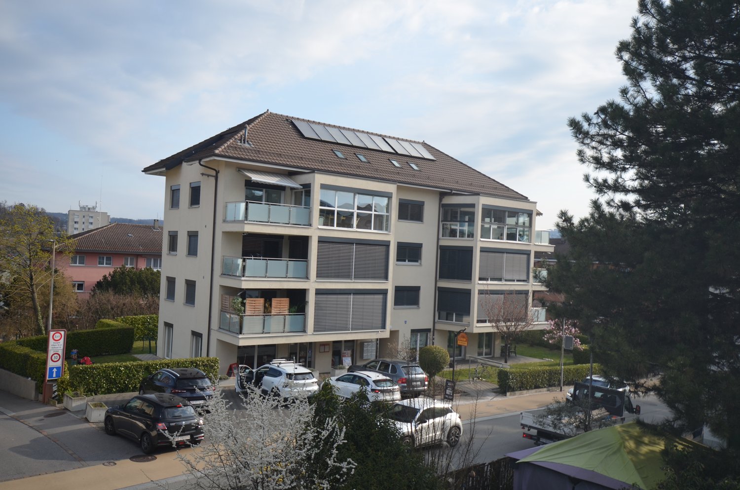 4 story building, solar panels on the roof, balconies, parking lot