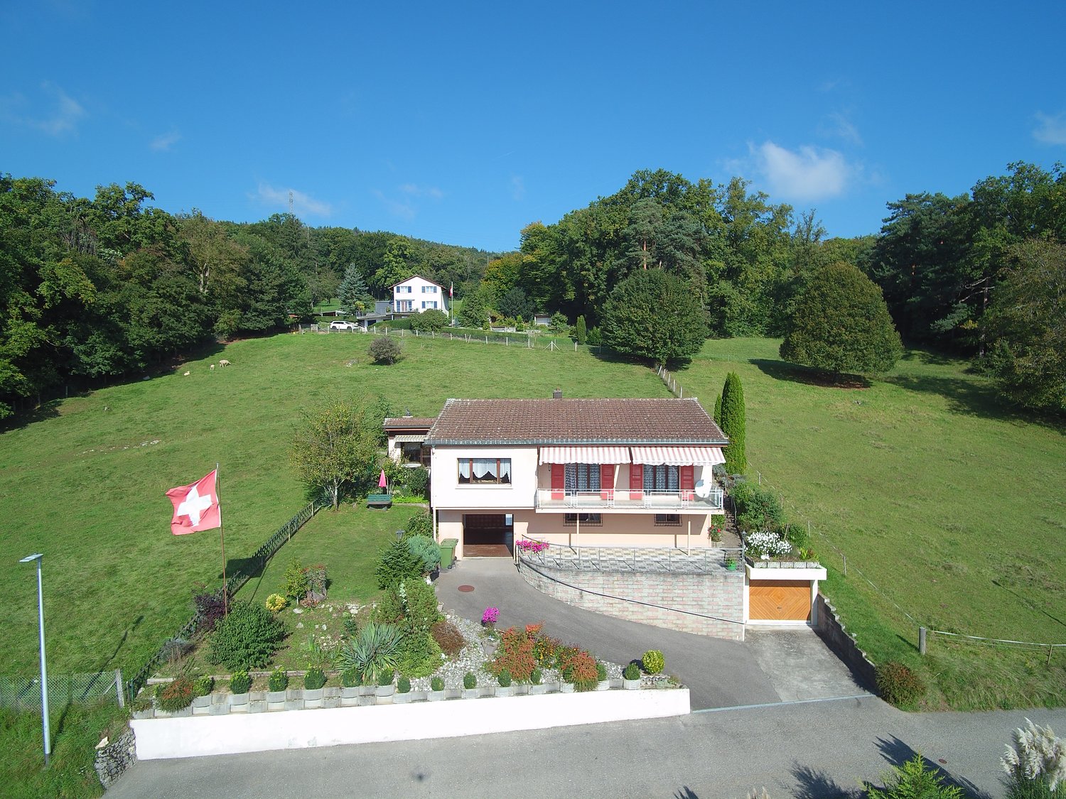 Detached house, brown roof, white walls, garage, balcony, surrounded by green grass, gardens, trees, Swiss flag