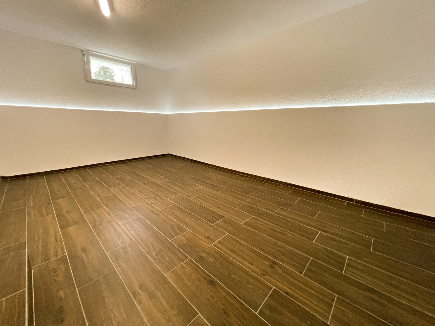 Empty room with wooden floor and white walls, window on one wall.
