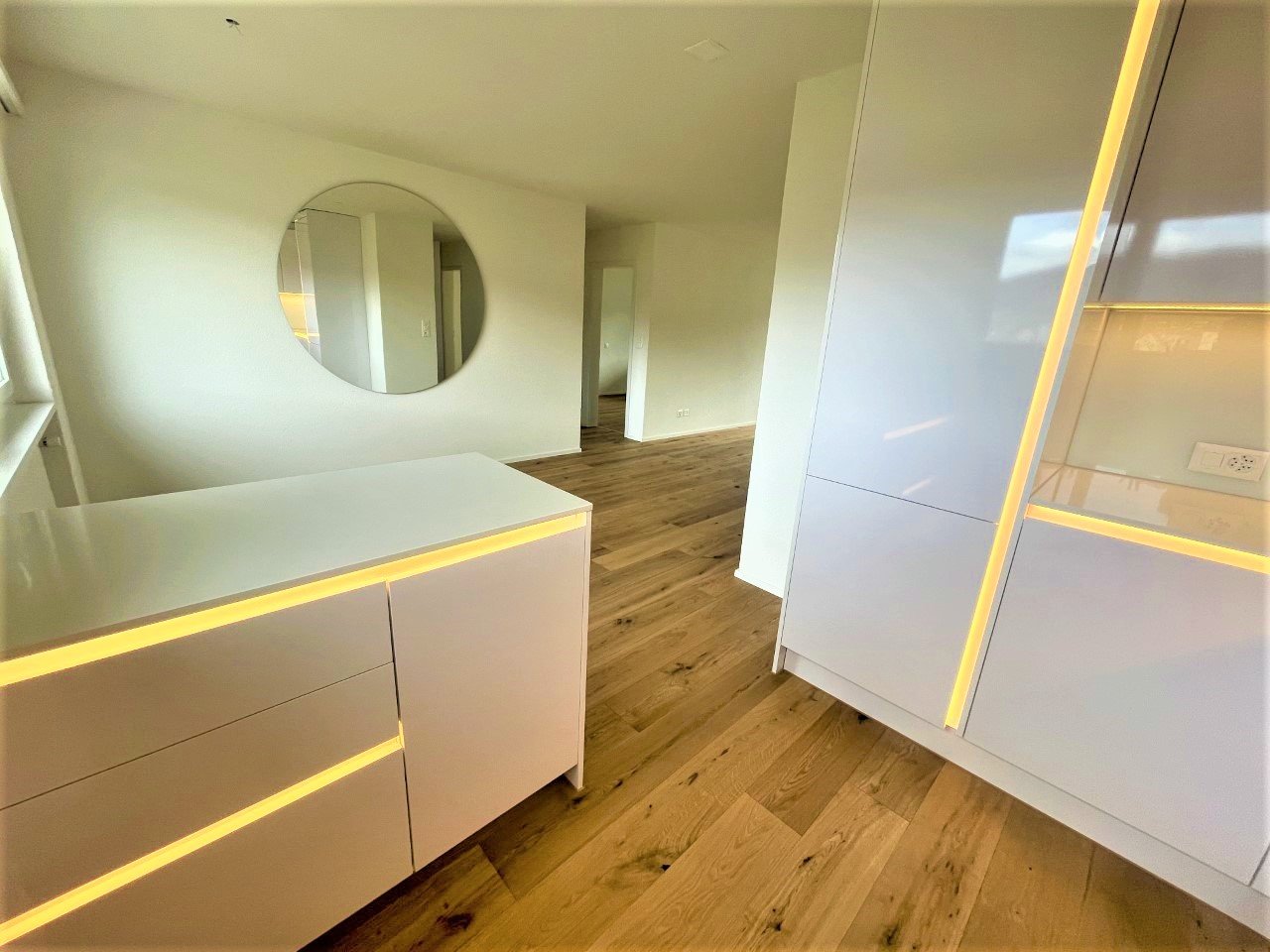 interior of bedroom with large round mirror, wooden floors, white cabinets, LED light strips, spacious