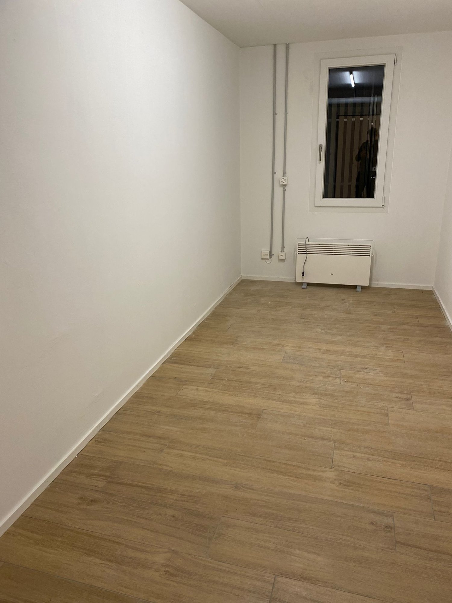 Empty room with wooden floors, white walls, an exit door with a glass panel, and an electrical outlet.