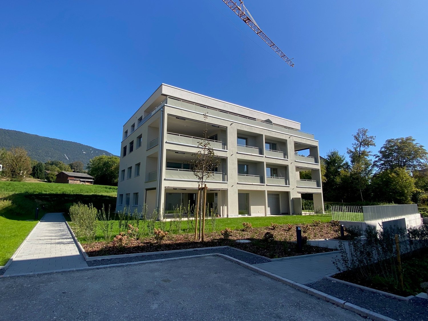white modern apartment building, multiple balconies, entrance gate, pathway, green area