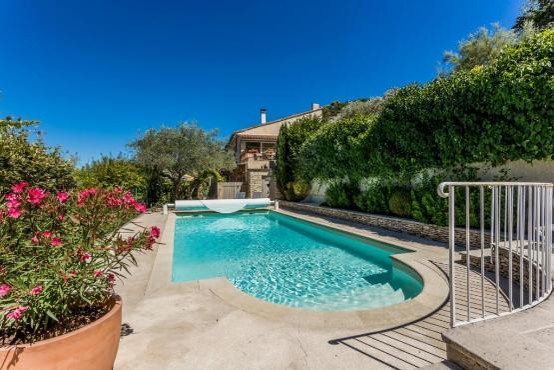 Swimming pool, stone wall, metal railing, plants, flowers, house in the background