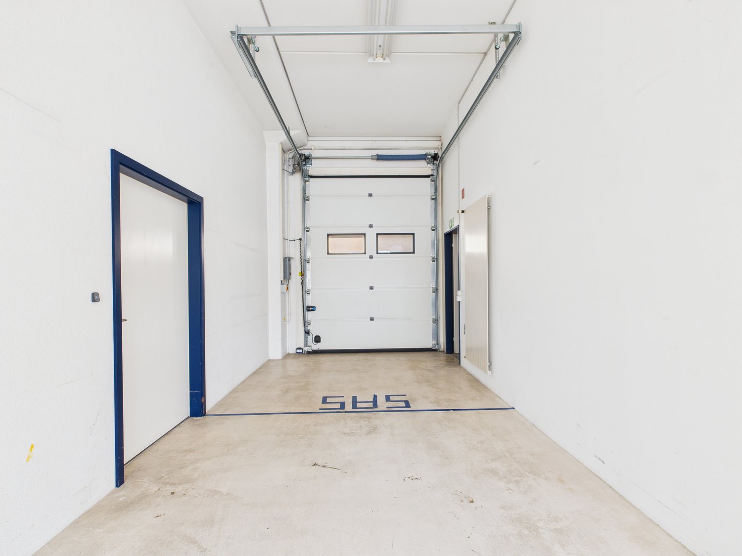 Empty storage room with concrete floor, white walls, blue trims on doors, two doors on left, two doors on right