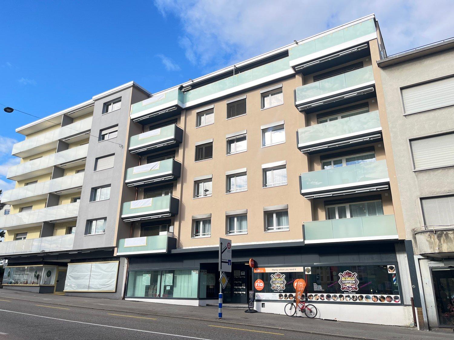 Apartment building with multiple stories and balconies, modern design with glass railings, located on a street with parked bicycle.