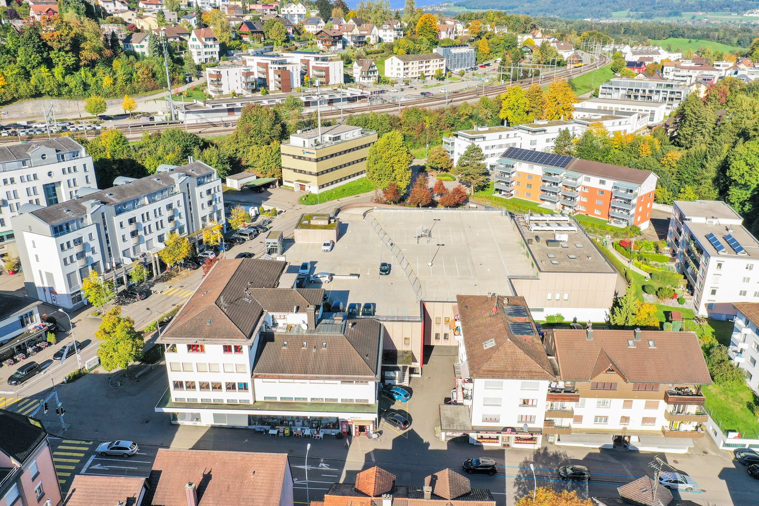 Several residential and commercial buildings, parking lots, solar panels, street and sidewalk, trees, green space
