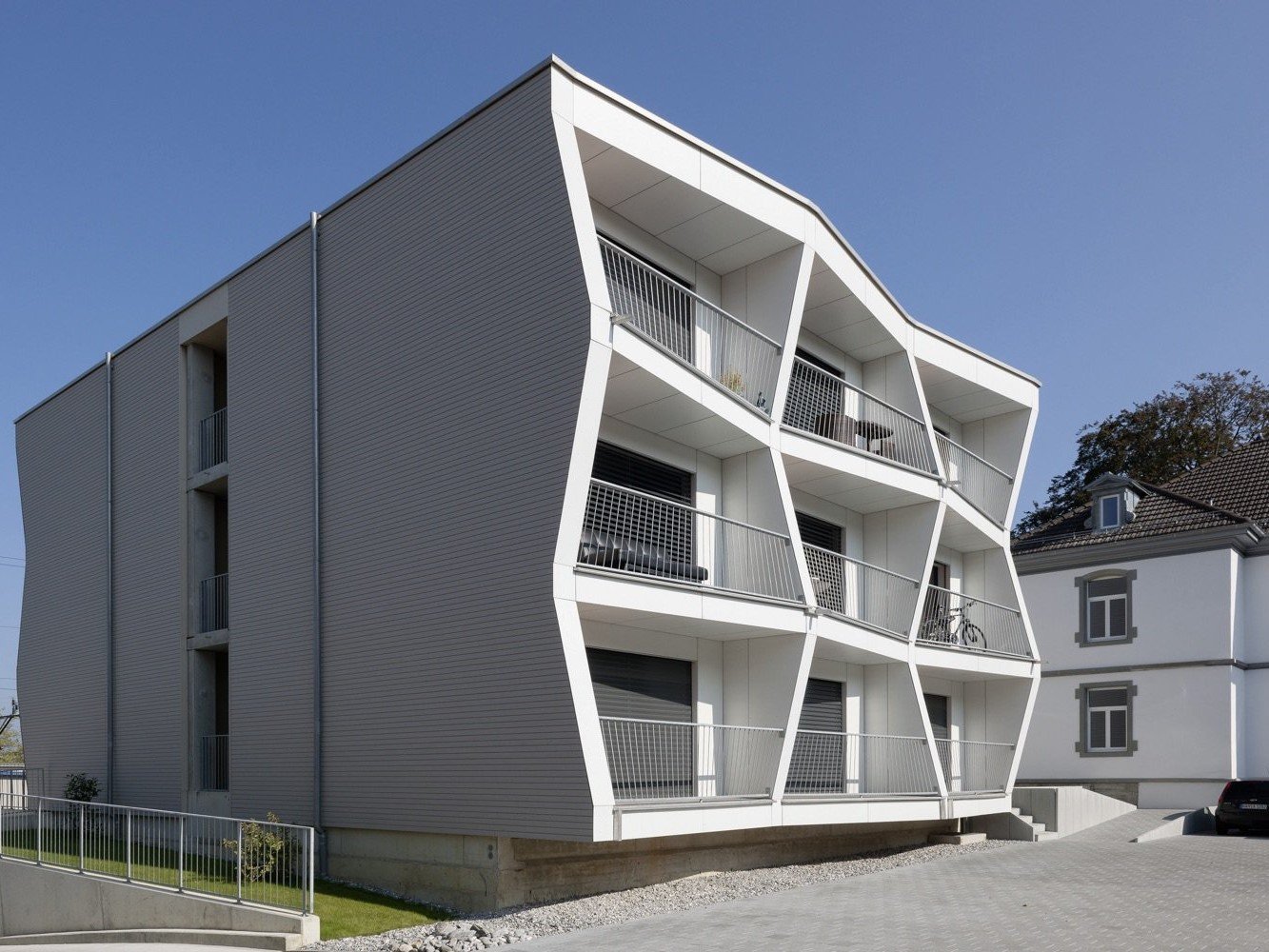 Modern apartment building, white exterior, slanted panels, multiple balconies