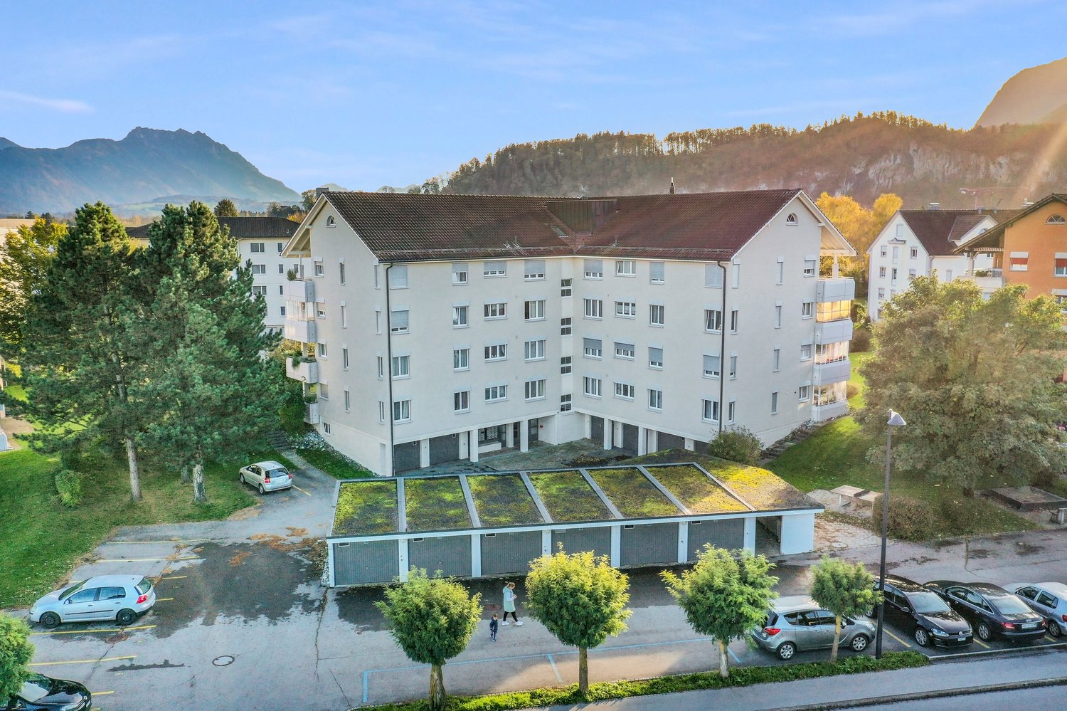Modern multistory building, multiple windows, garage with green roof, parking lots with several cars