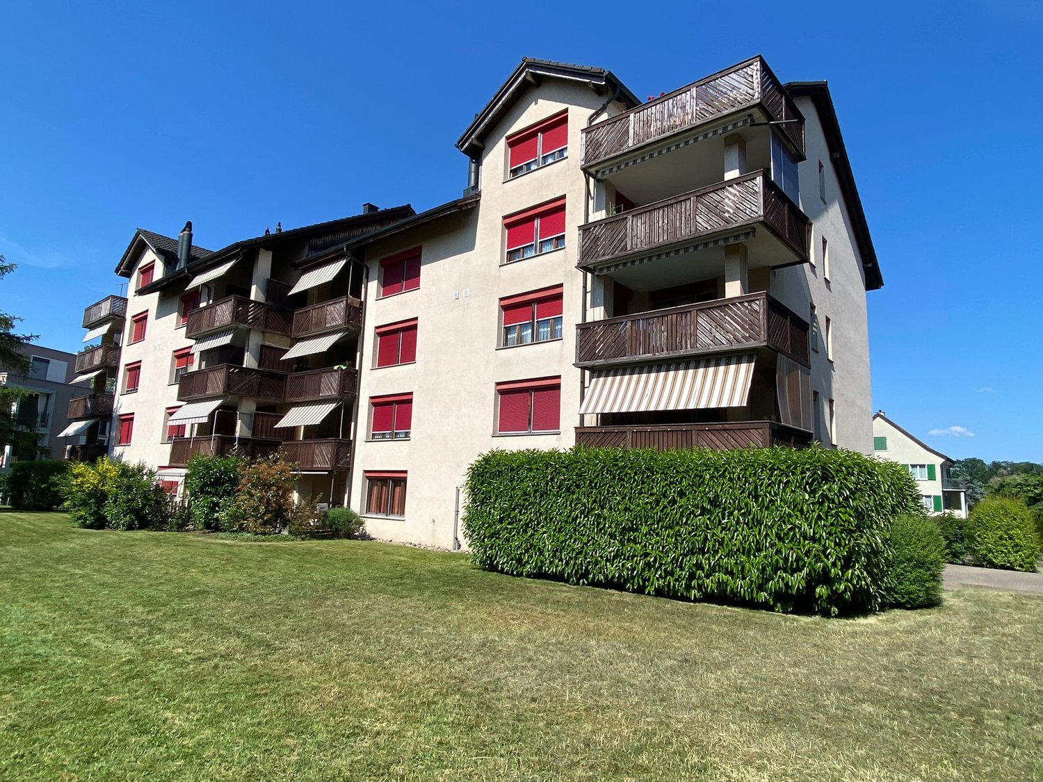 Multi-story apartment building, balconies, multiple floors, manicured lawn, bushes, blue sky