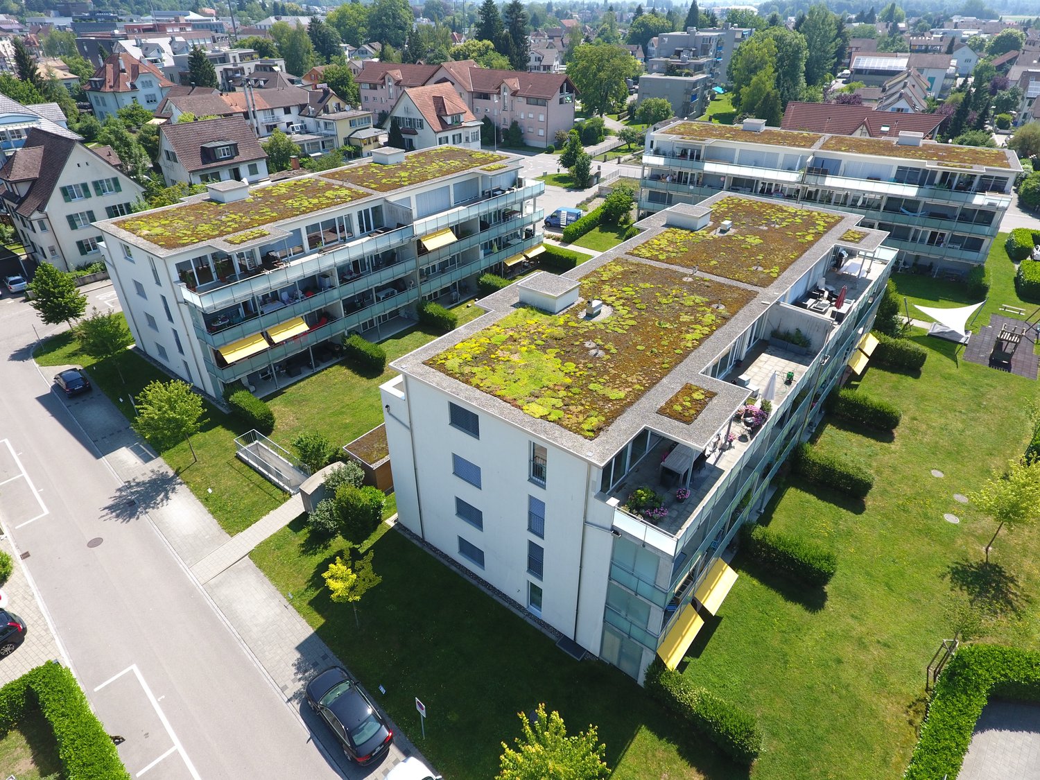 White apartment building with green roof, yellow awnings, several windows, and a parking area in front