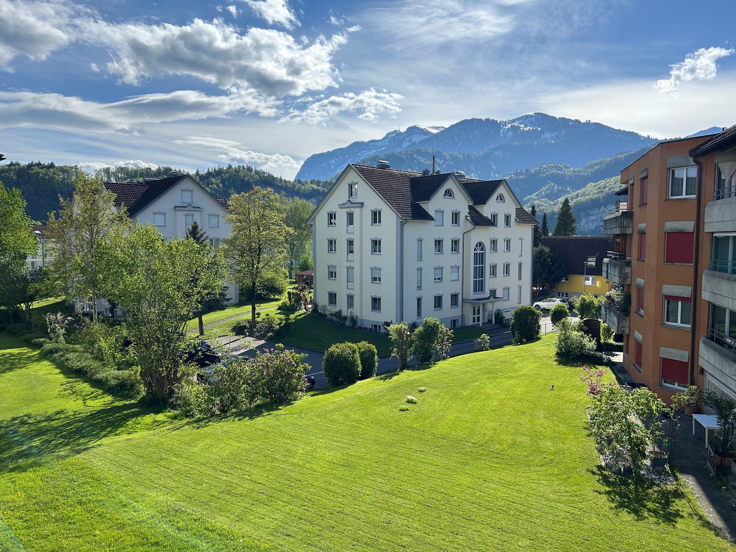 Apartment complex in a rural area, mountain views, well-maintained garden, car parked outside