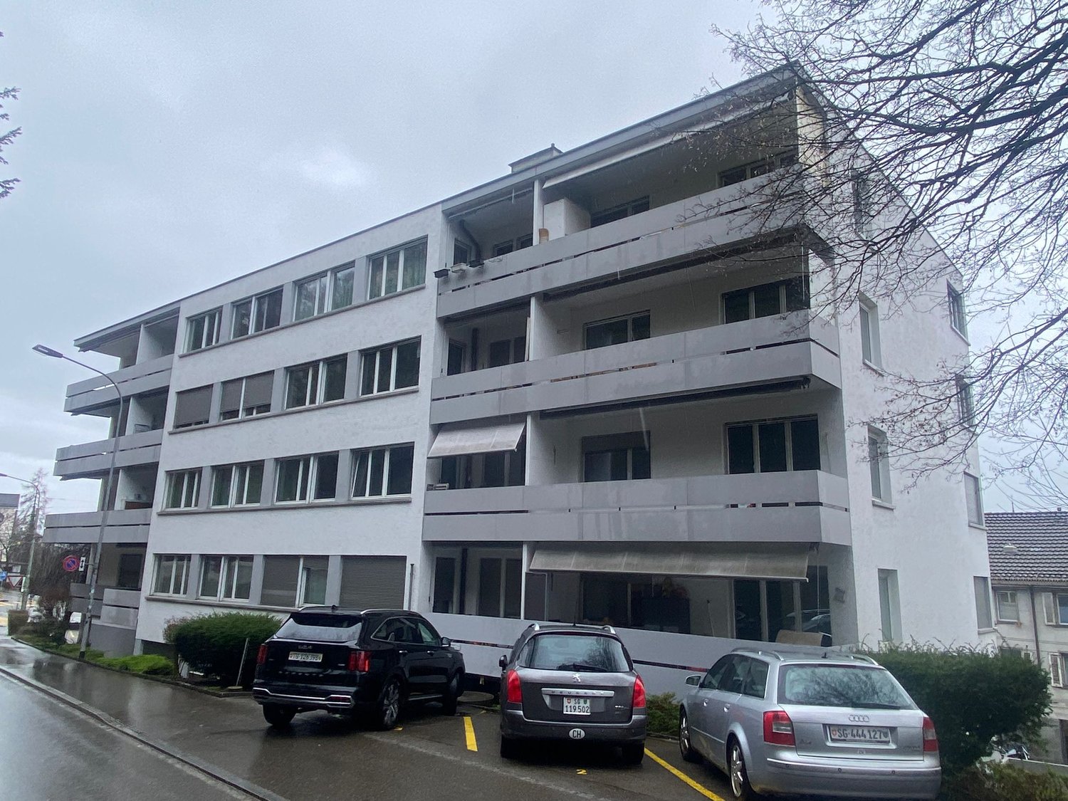 White building, 3 floors, balconies, cars parked in front, street light