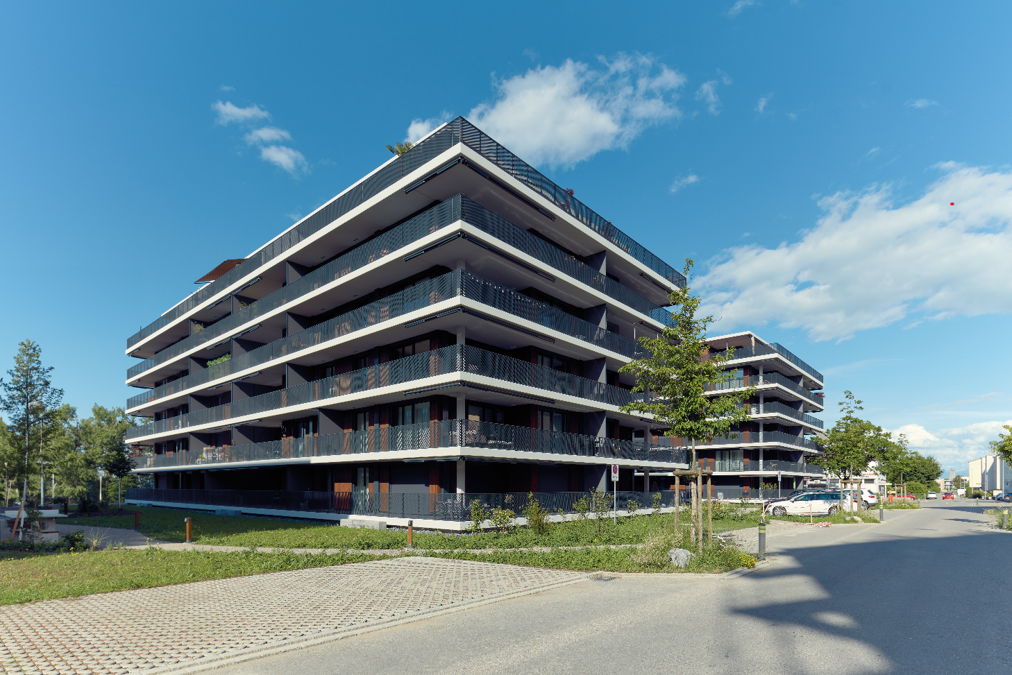 modern multi-story building, glass balconies, brick walls, grassy areas, clear sky, no parking visible