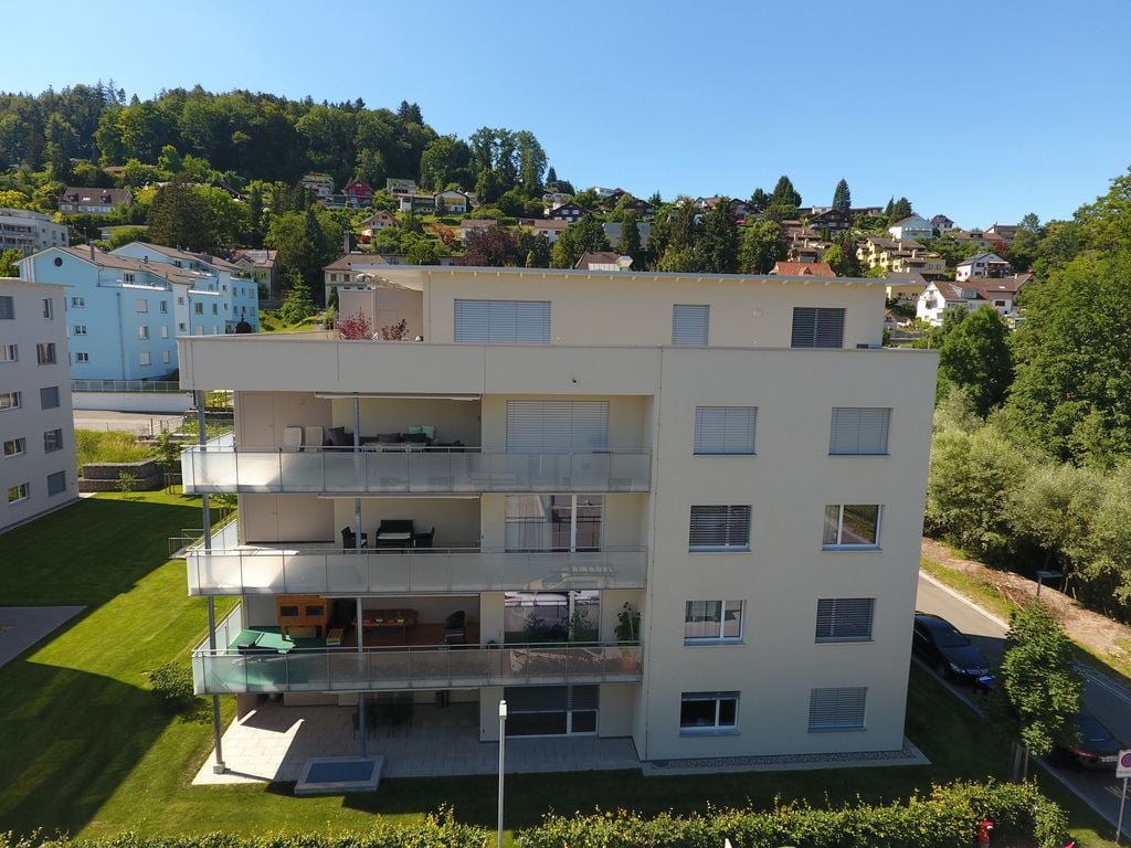 4 story apartment building, beige exterior, large balconies, mountain view, trees, road, parking lot