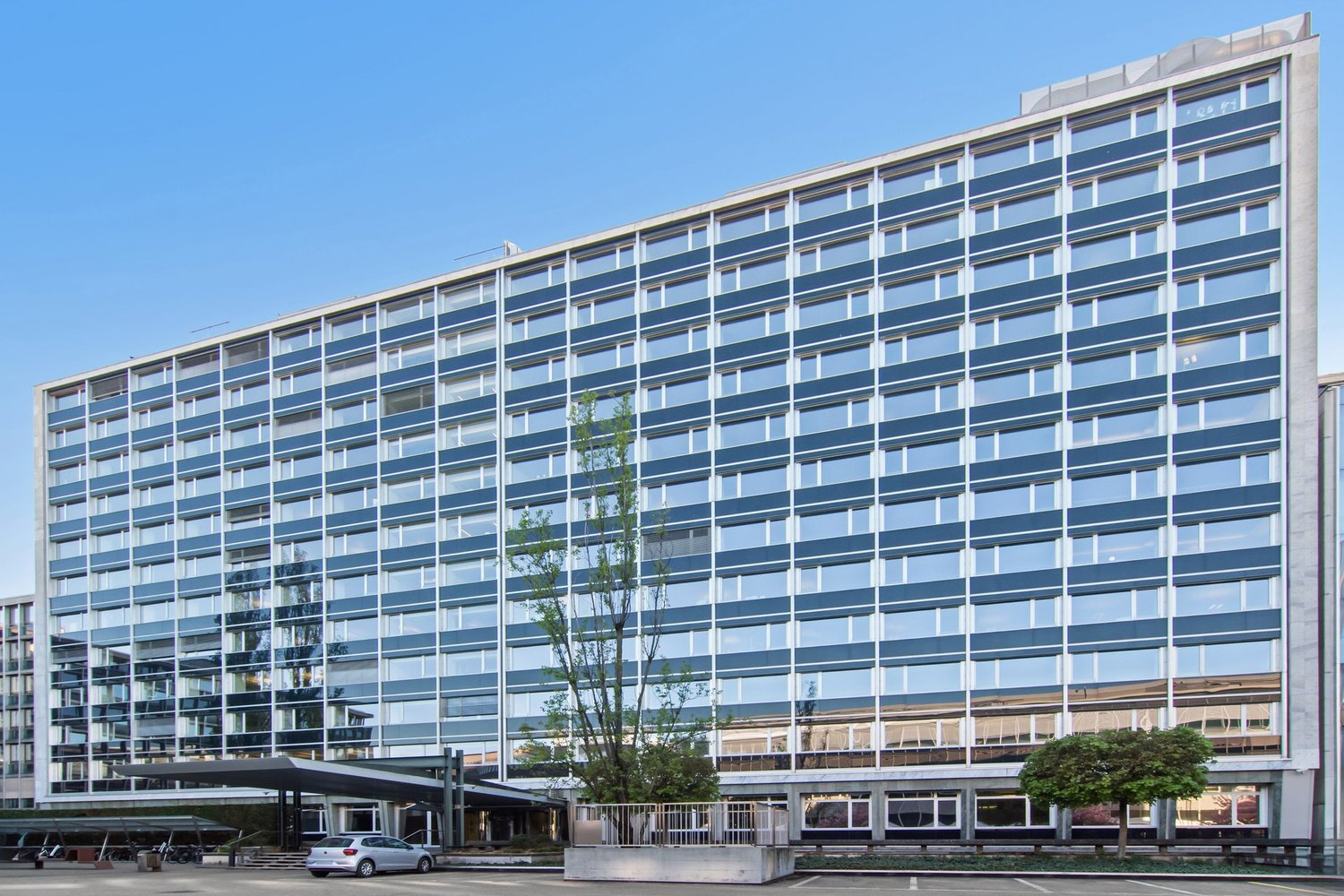 modern office building, multiple floors, glass windows, car parked in front