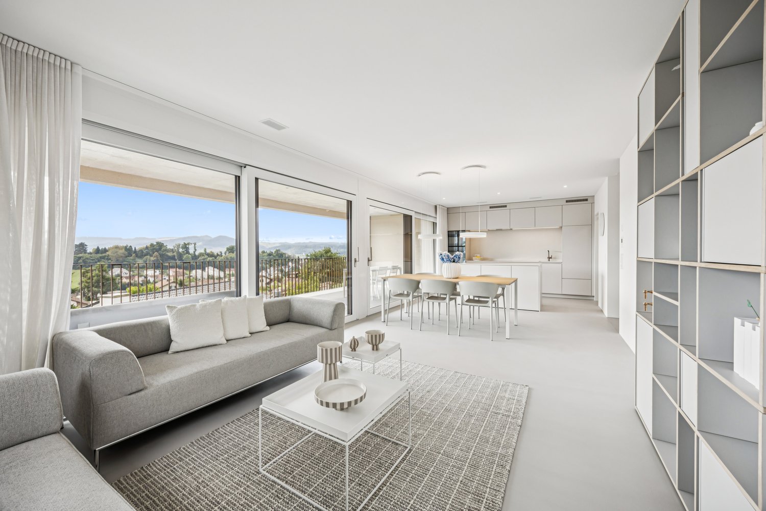 modern living room with gray sofa, white coffee table, dining area, balcony, sliding windows with view