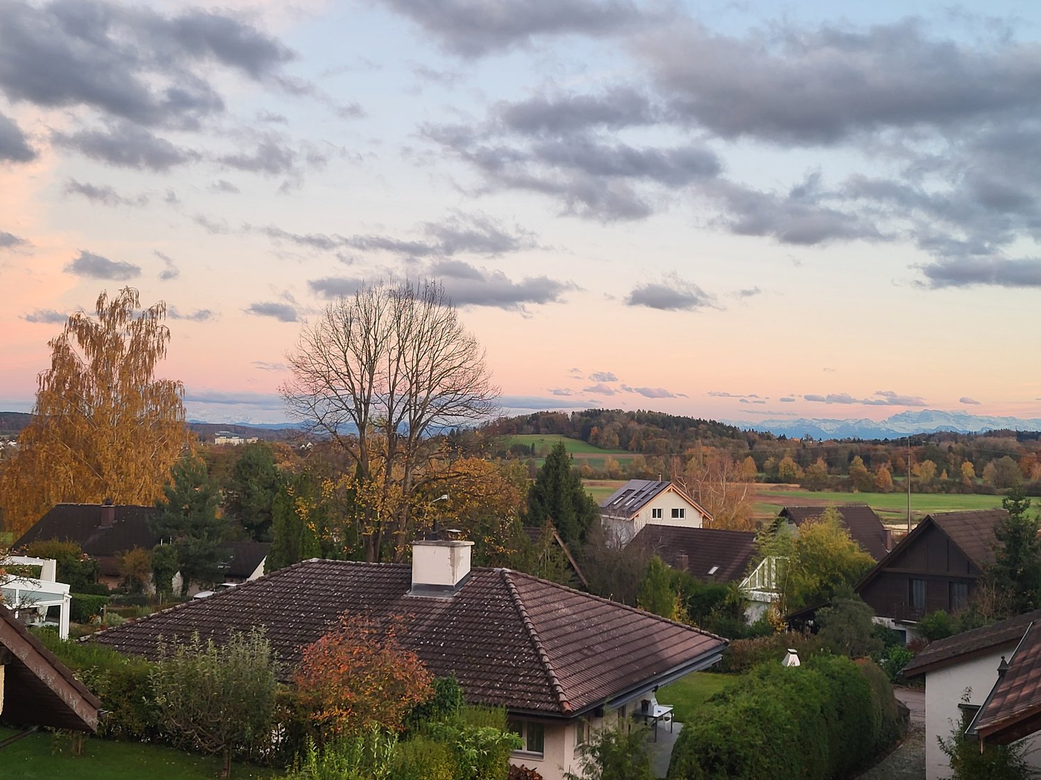 House with brown roof and chimney, white walls, set on a hillside with trees and a beautiful view of the mountains