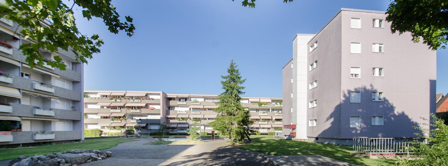 two high-rise apartment buildings, several balconies, trees, garden, grass, street