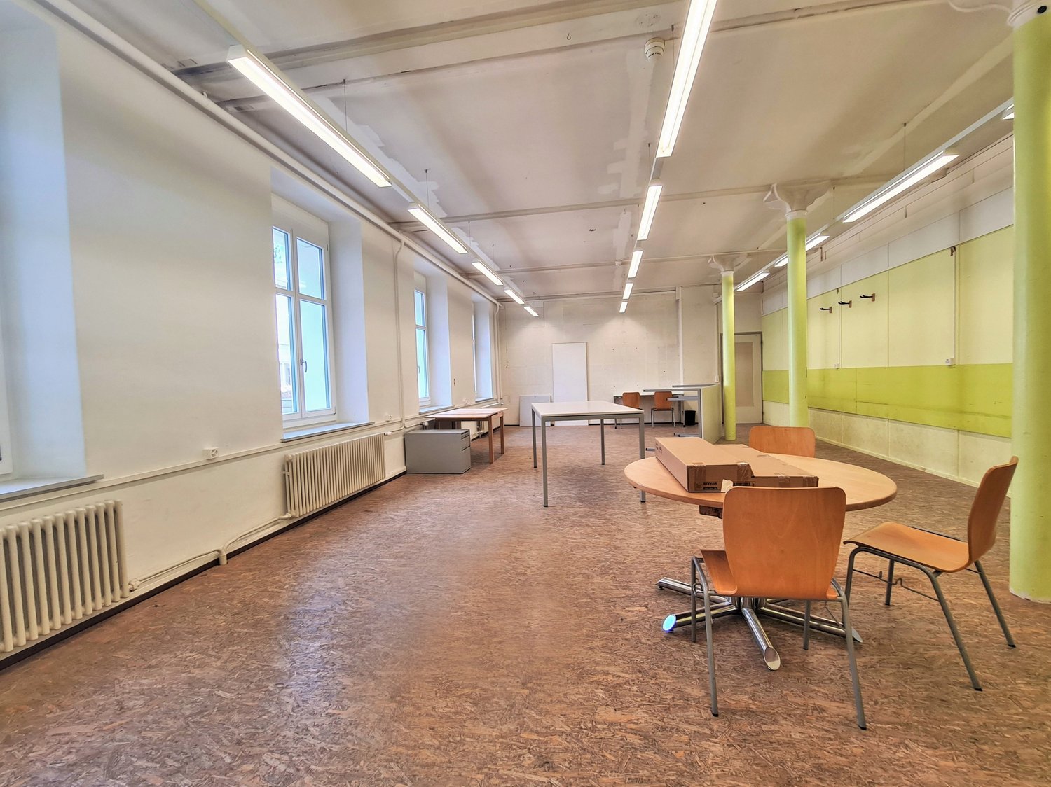 empty office with wooden floor, white walls, radiators, large windows, round and rectangular tables, chairs