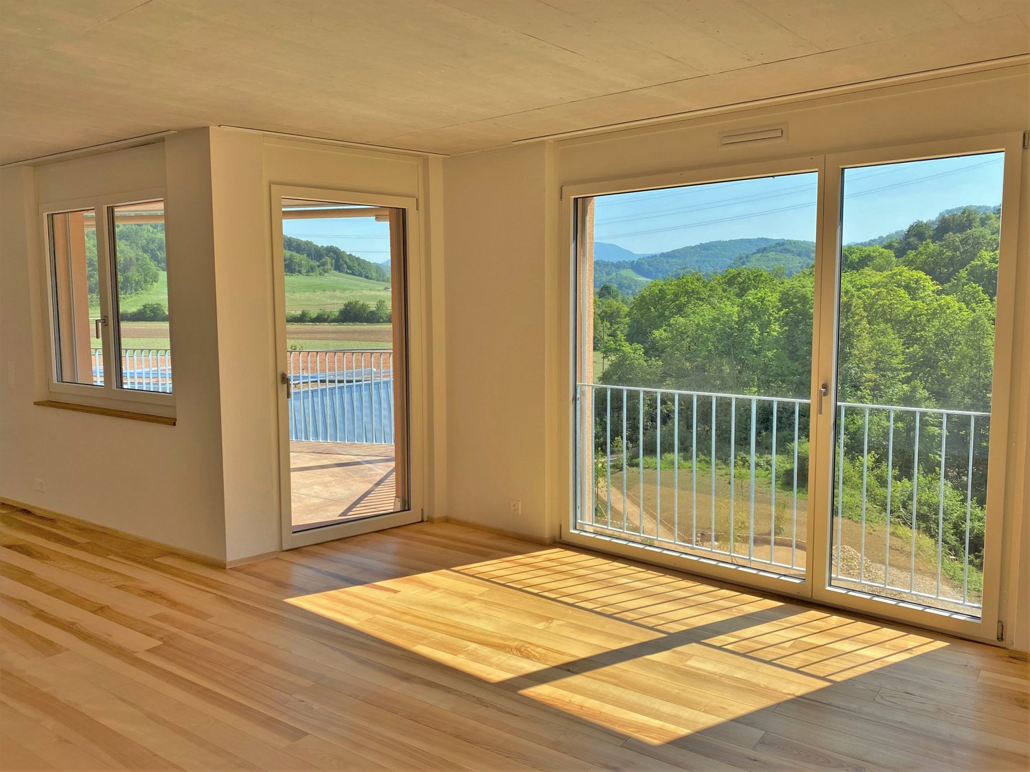 large room, wooden floors, sliding glass doors to balcony, wide view