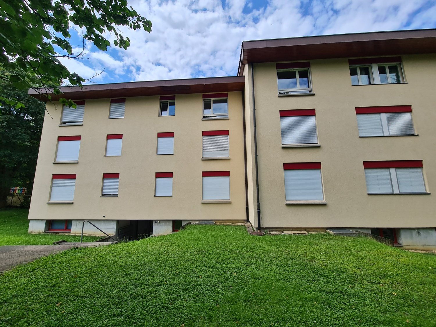 Two story building with 16 windows, red accents, raised ground floor, walkway leading to entrance