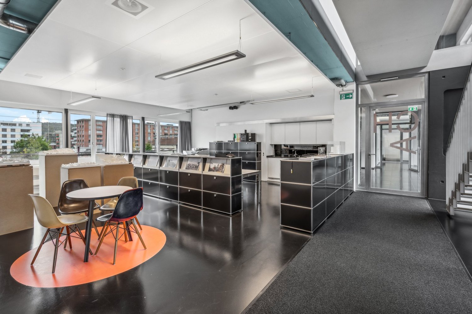modern interior design with white walls, large windows, black flooring, grey carpeting, modern seating, long tables, built-in cabinets, office equipment