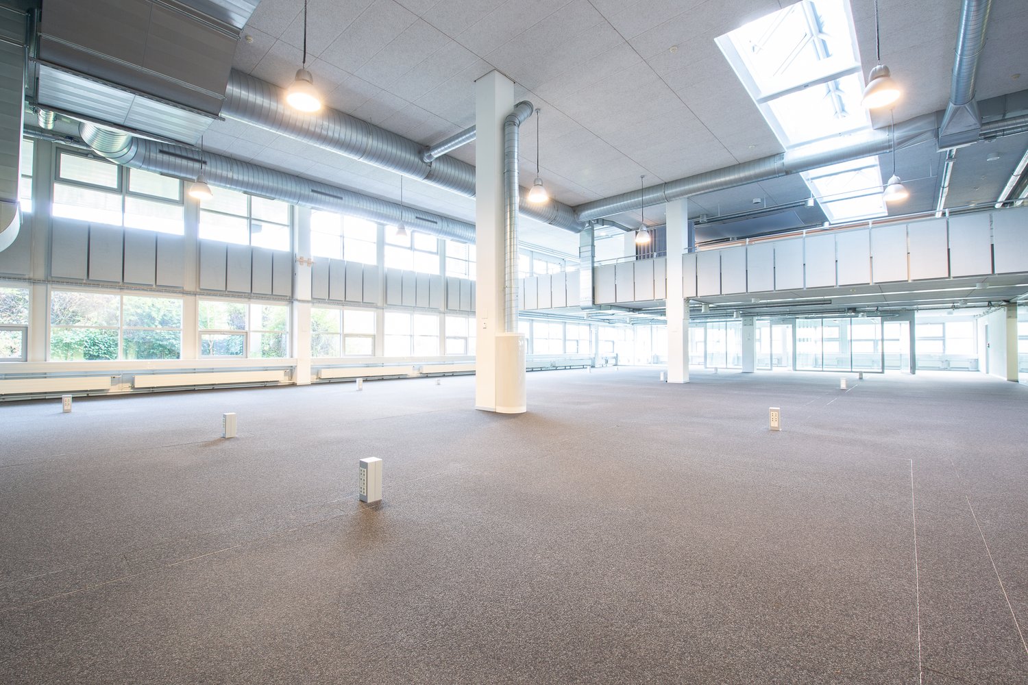 Wide open space, large windows, hanging lamps, central column, balcony with railings, metal ducts on ceiling