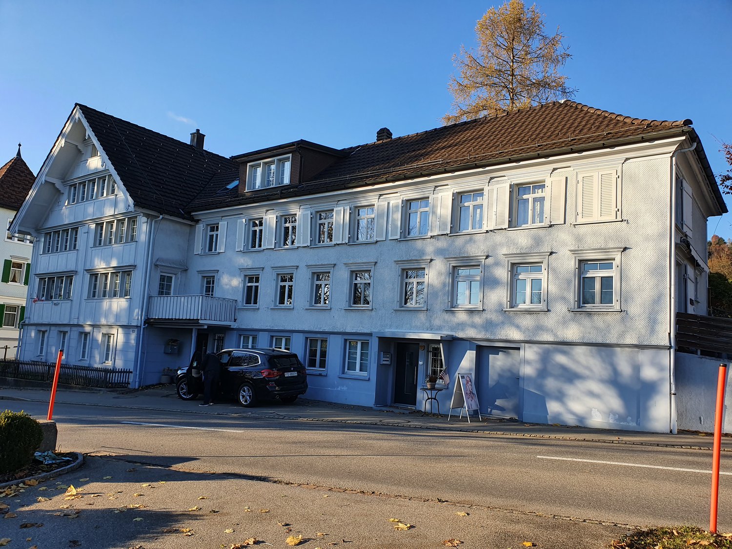 white painted exterior, many windows, small balcony on the second floor, black car parked in front