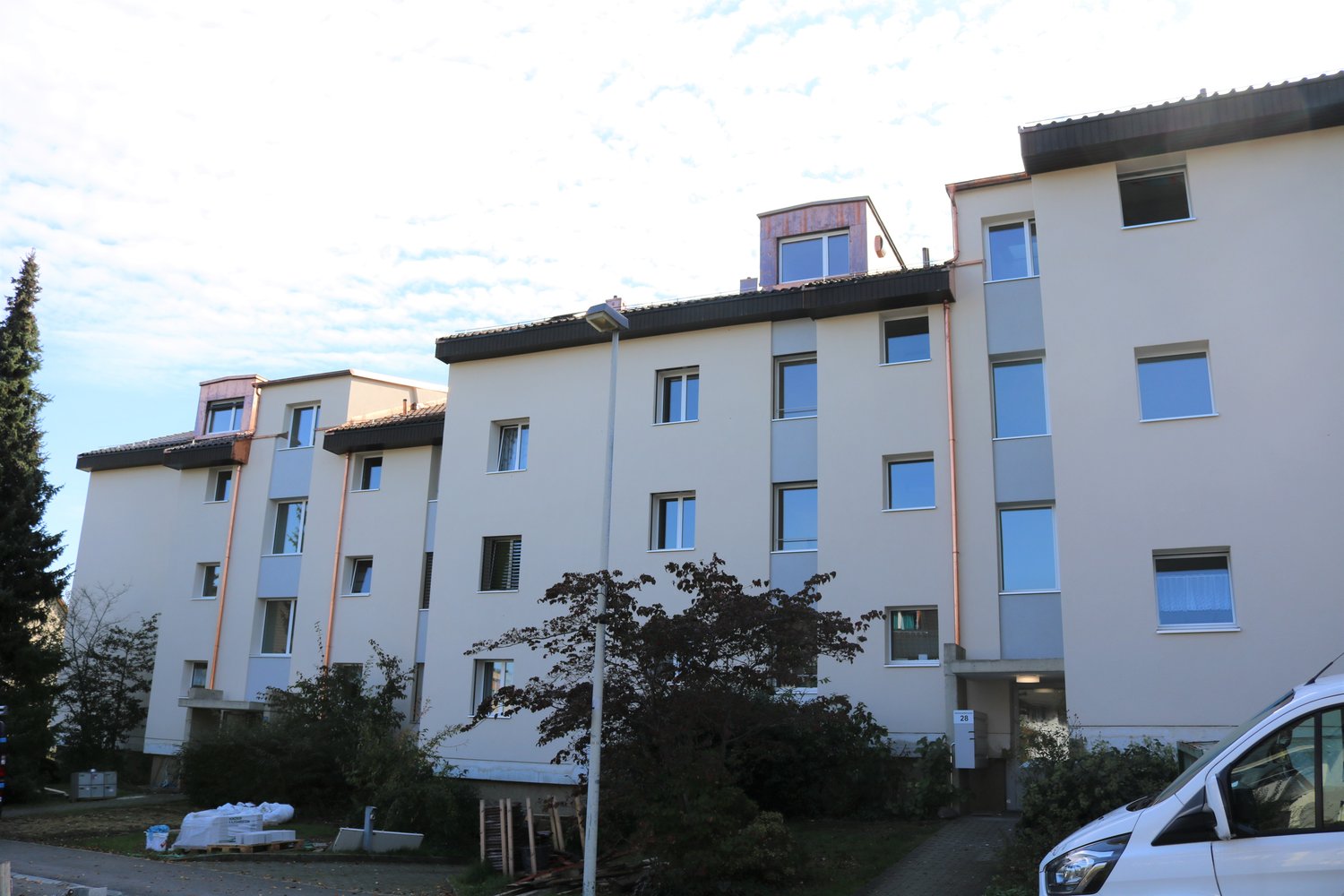 modern apartment building, white exterior, large windows, several floors, roof terrace, entrance on ground floor, landscaping in the front