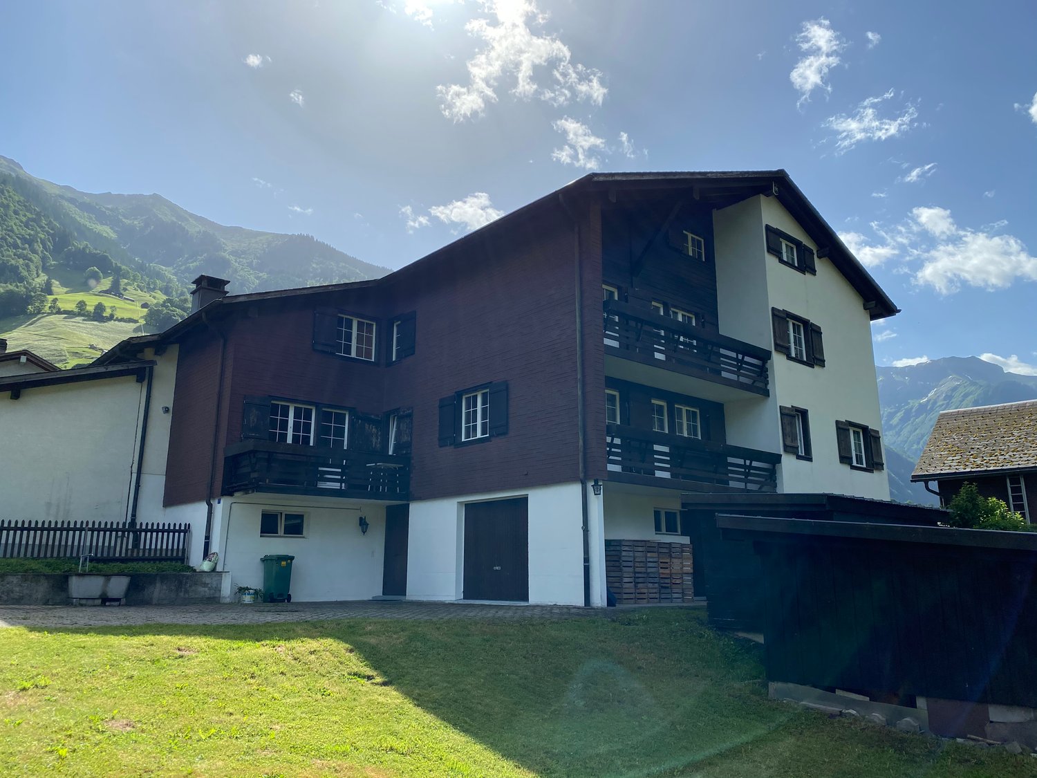 3-story chalet, brown wood and white walls, multiple balconies, garage, grassy lawn, mountain background