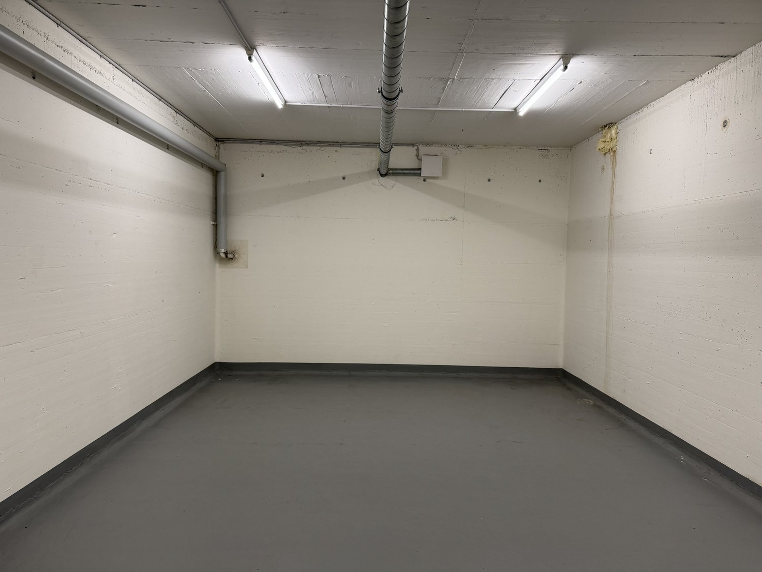 Empty room with white walls and concrete floor. Pipes are on the ceiling and one of the walls