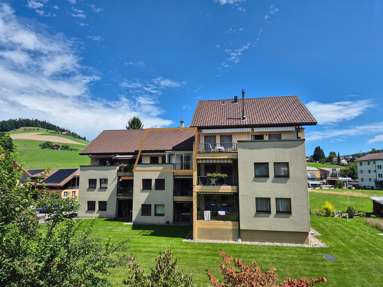 Two story apartment building, brown roofs, balconies, windows with awnings, located on a hill with green lawn
