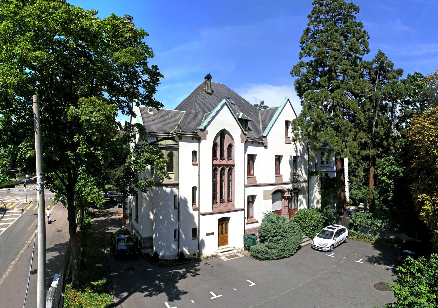 3 story white house, grey roof, arched windows, main door, large yard, parking