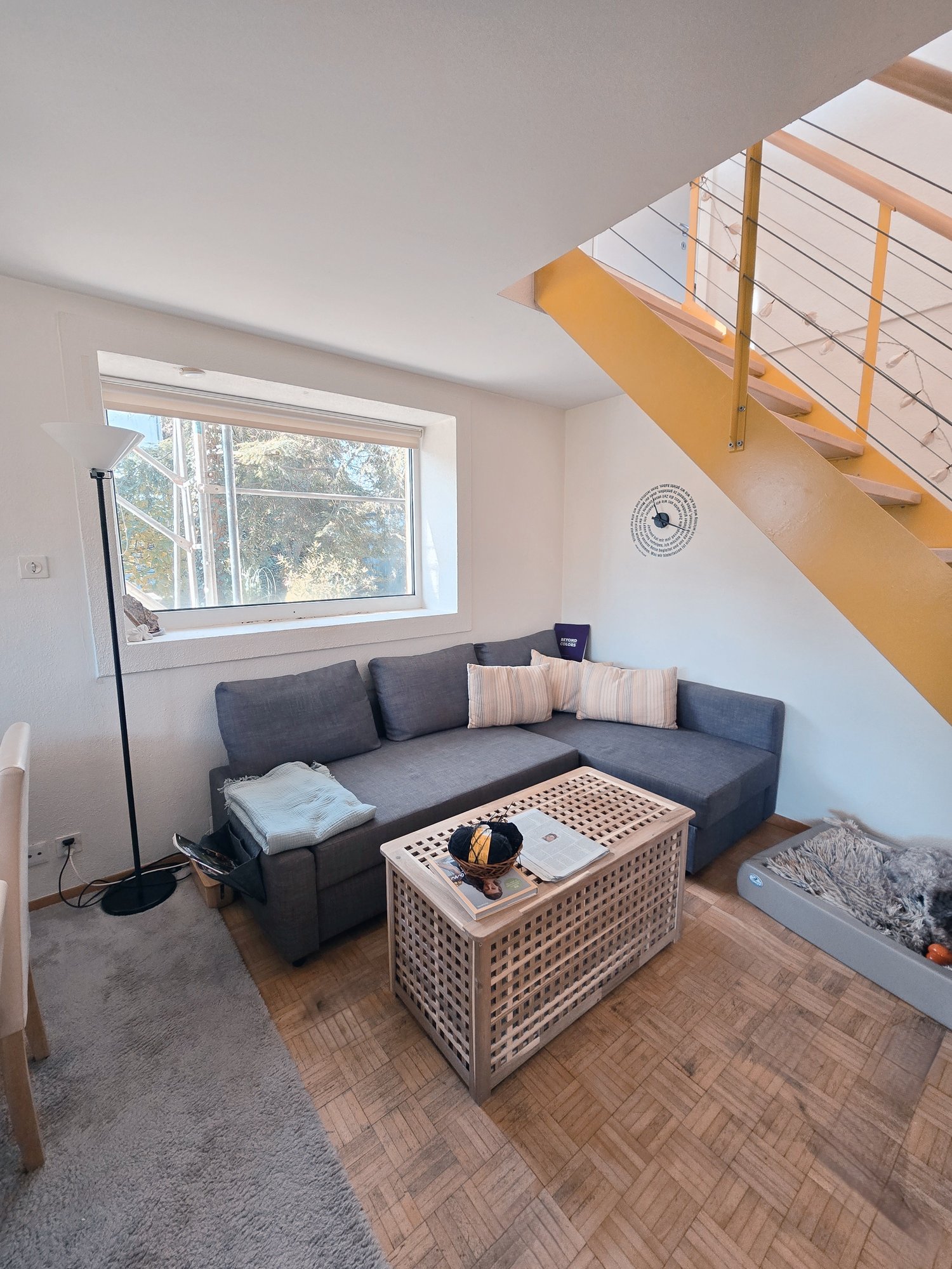 sofa with cushions, coffee table, a desk with books, a chair, a lamp, a power outlet