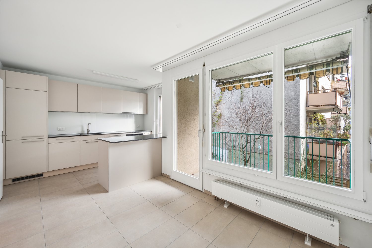 Open kitchen, tile floor, large windows with balcony, white cabinets, island countertop