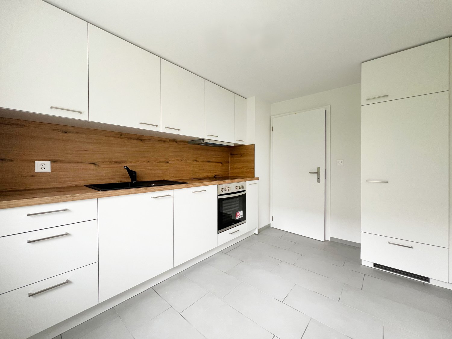 White cabinetry, wooden countertop, white tile flooring, built-in oven, under-cabinet lighting, wall socket, stainless steel sink, and faucet