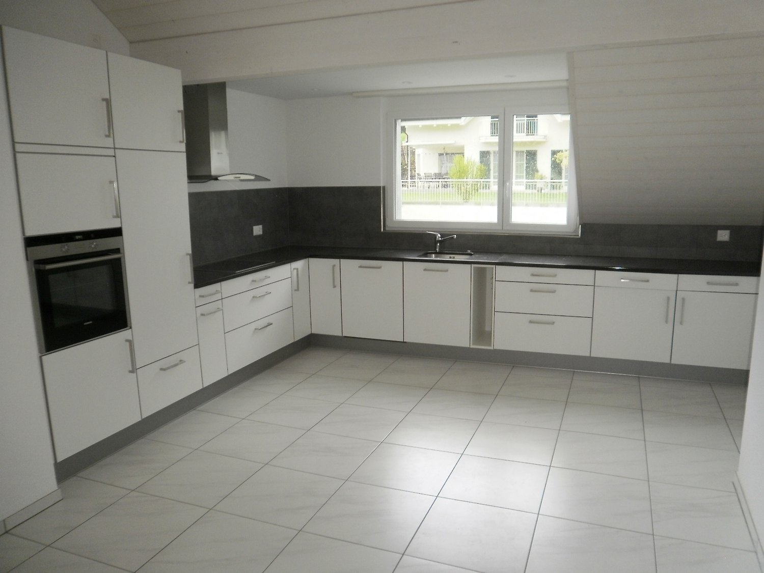 a kitchen with modern white kitchen cabinetry, tiled flooring, modern sink and black countertops