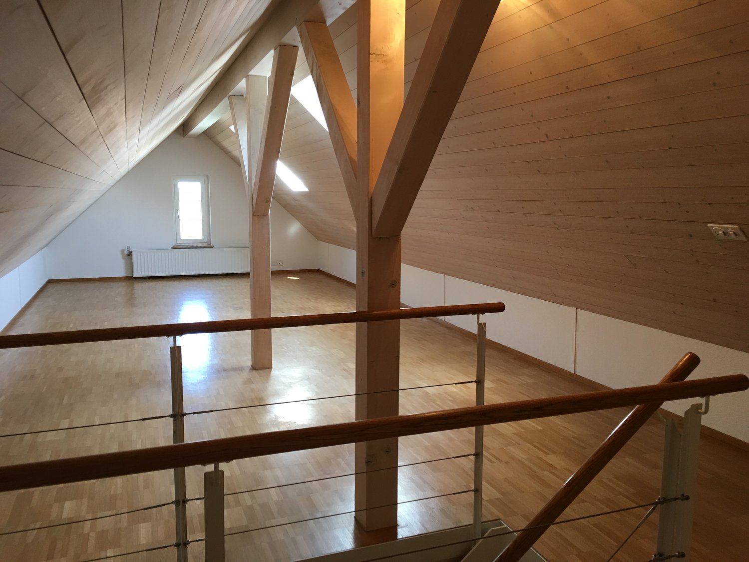 Empty attic with wooden flooring, wooden ceiling and railing, white walls, 2 windows