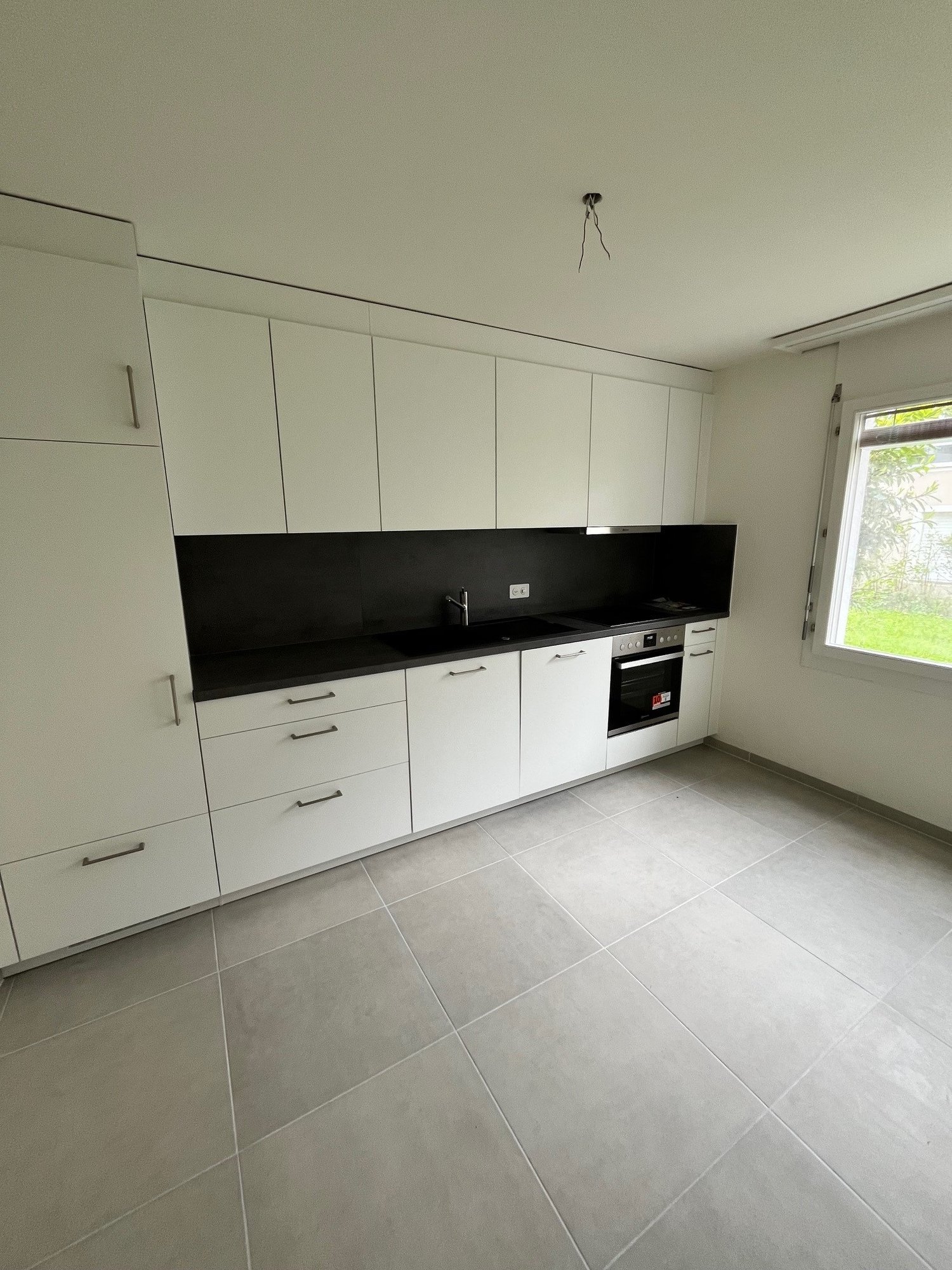 white cabinets, black countertops, stainless steel sink, built-in oven, window