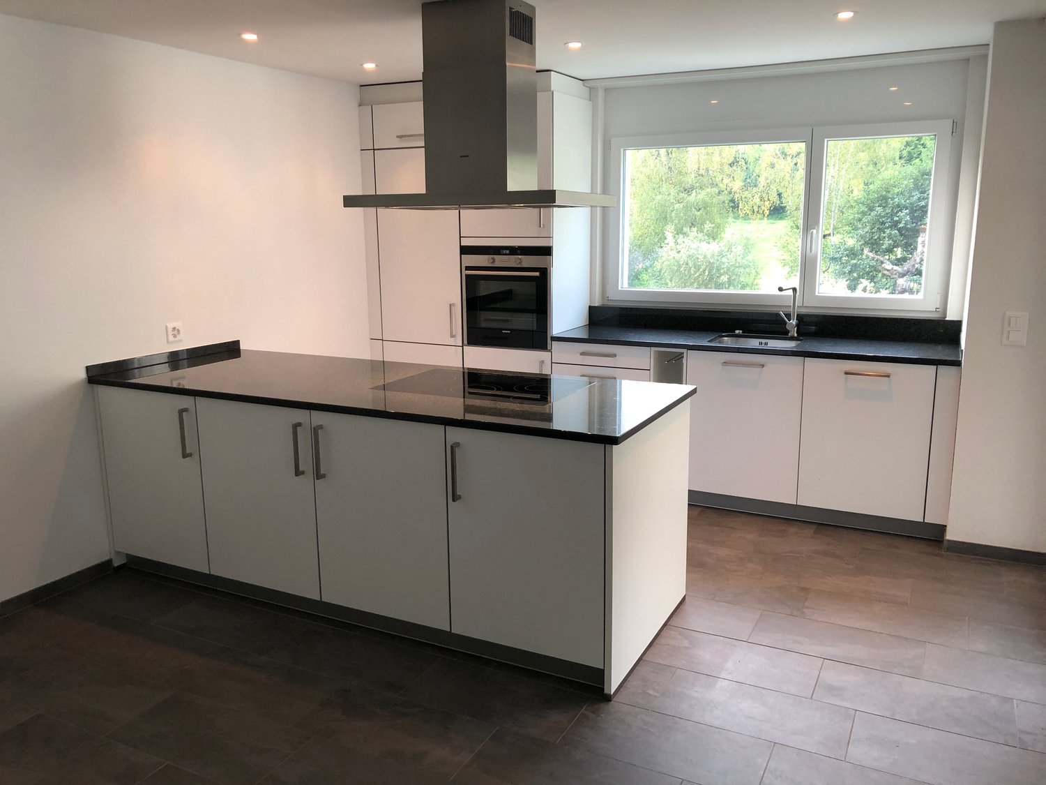 modern kitchen with white cabinets, black countertops, central island, gas stove, oven, range hood, sink, dishwasher, windows