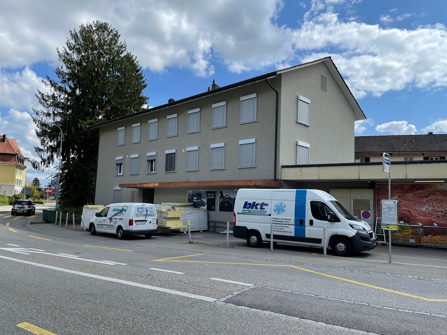 3 story building, grey exterior, multiple windows, awning, 2 vans parked in front