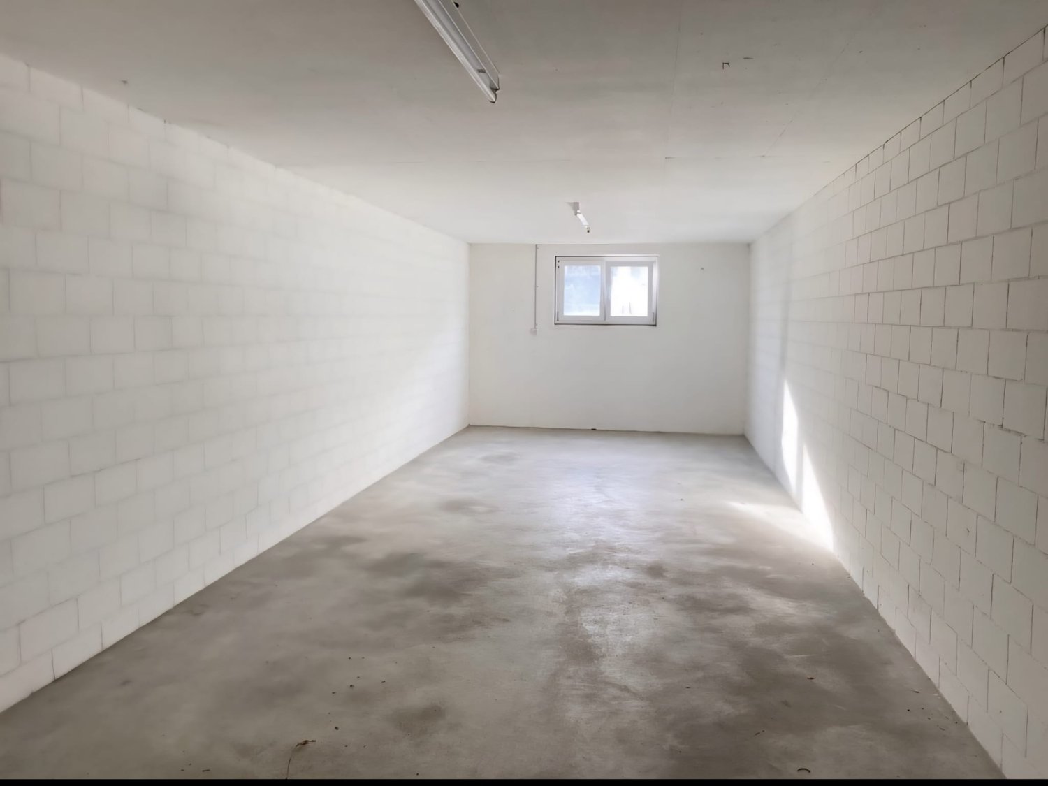 empty room with white brick walls, concrete floor, small window