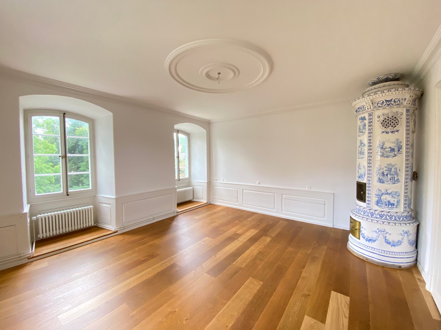 wooden floor, white walls, arched window, blue and white fireplace, white radiator, circular ceiling, two arch windows