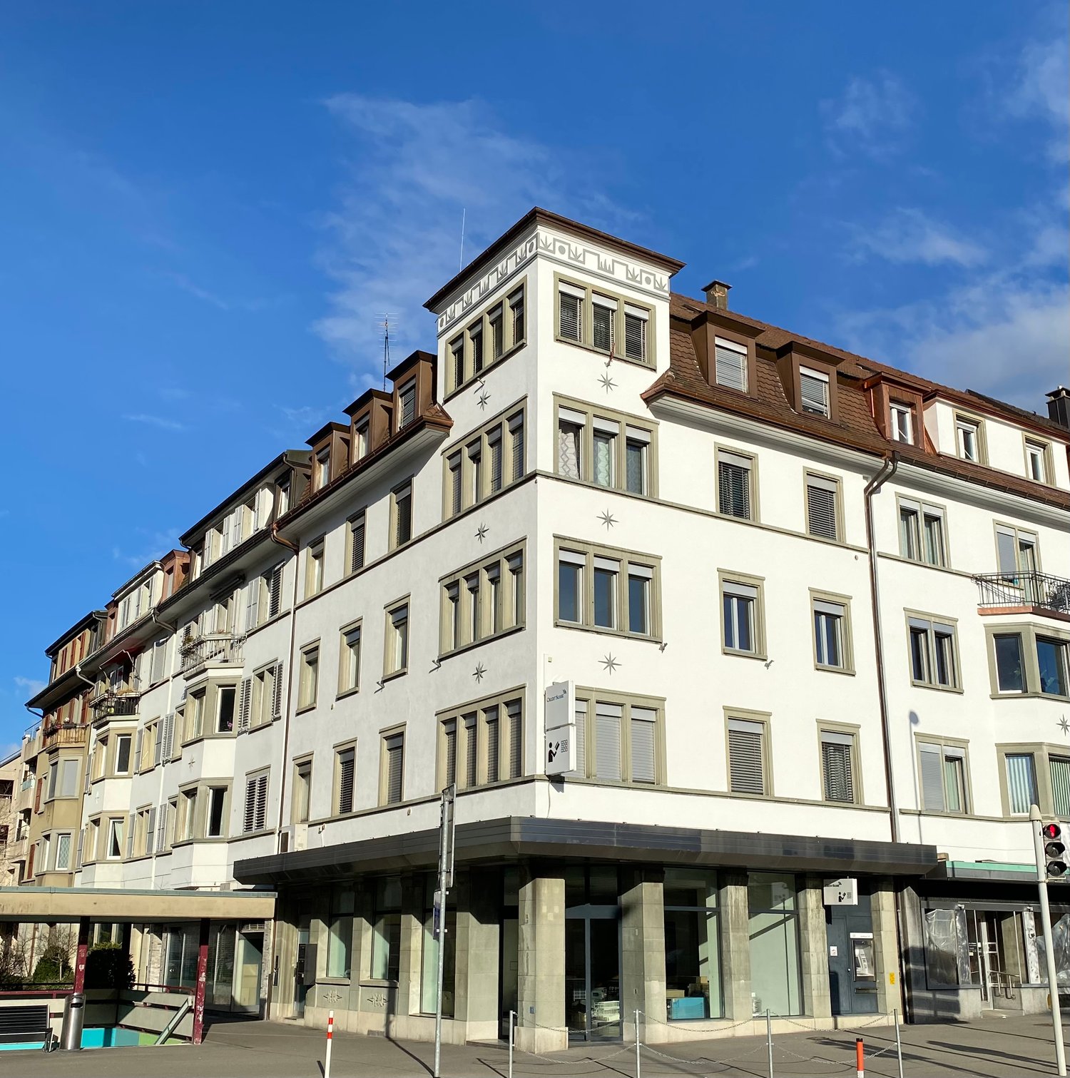 6 story building, white walls, many windows, brown roof, 2 balconies on the top floor