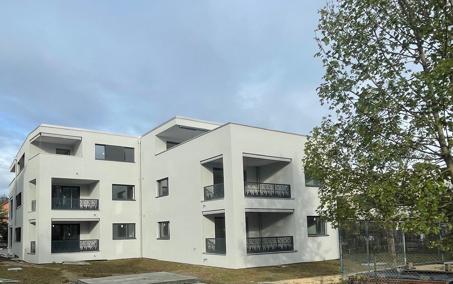 3-story modern apartment building with white exterior, balconies, and large windows