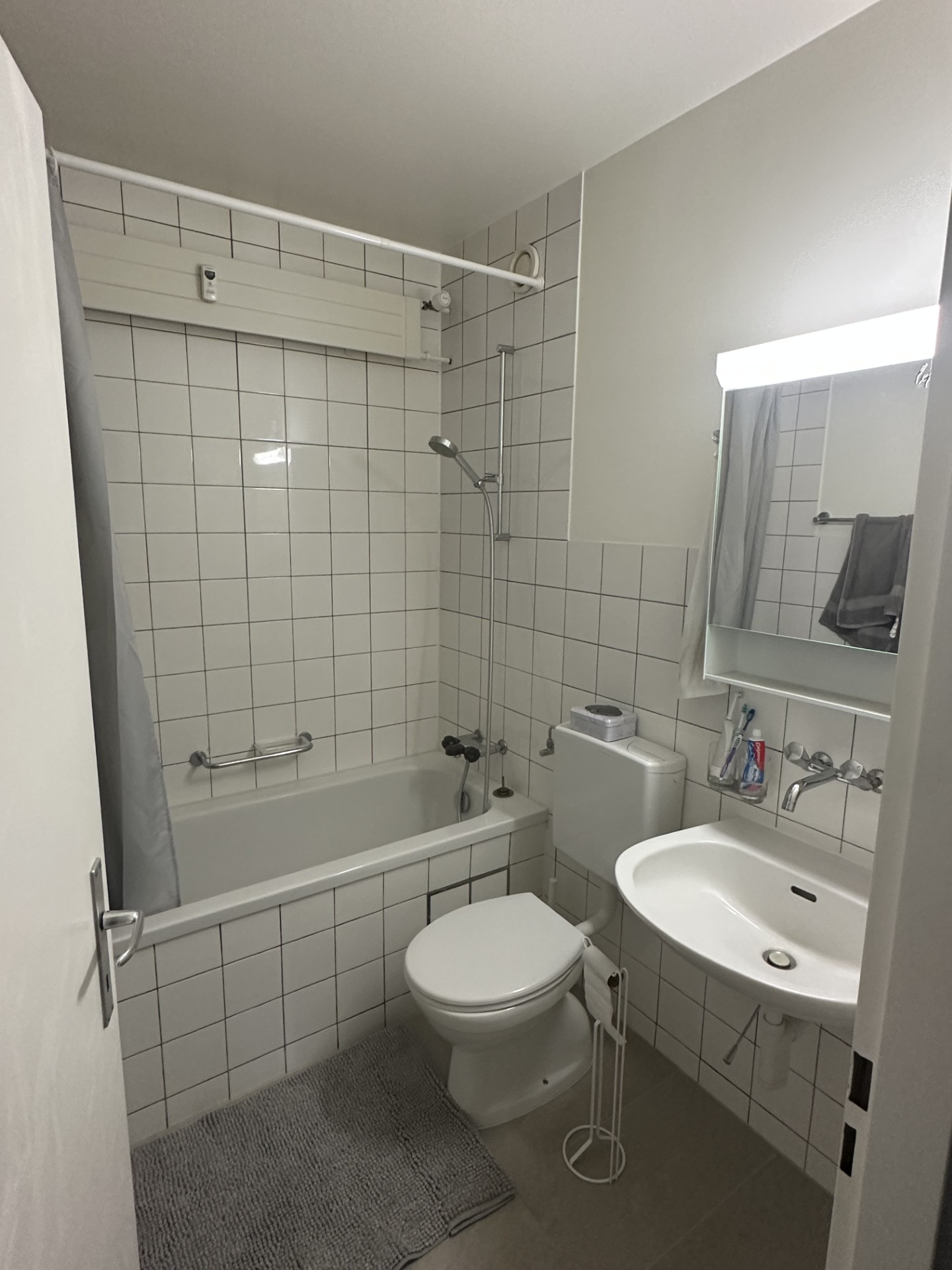 Bathroom with white tiles, bathtub, toilet, sink, mirror, shower head, and towel rack