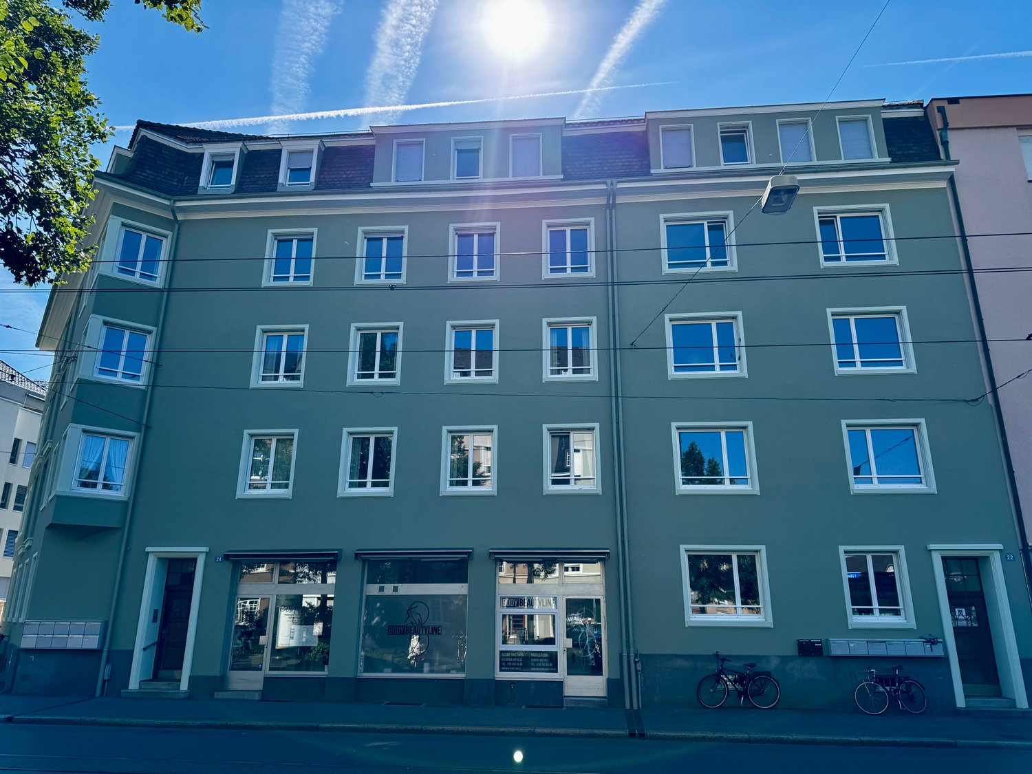 4 story building with many windows, green paint, storefronts at street level, bicycles parked in front