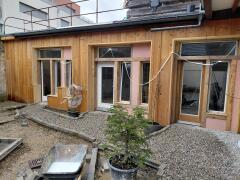 Wooden exterior, pink painted wall, 3 windows, balcony on top floor, gravel driveway, partially completed
