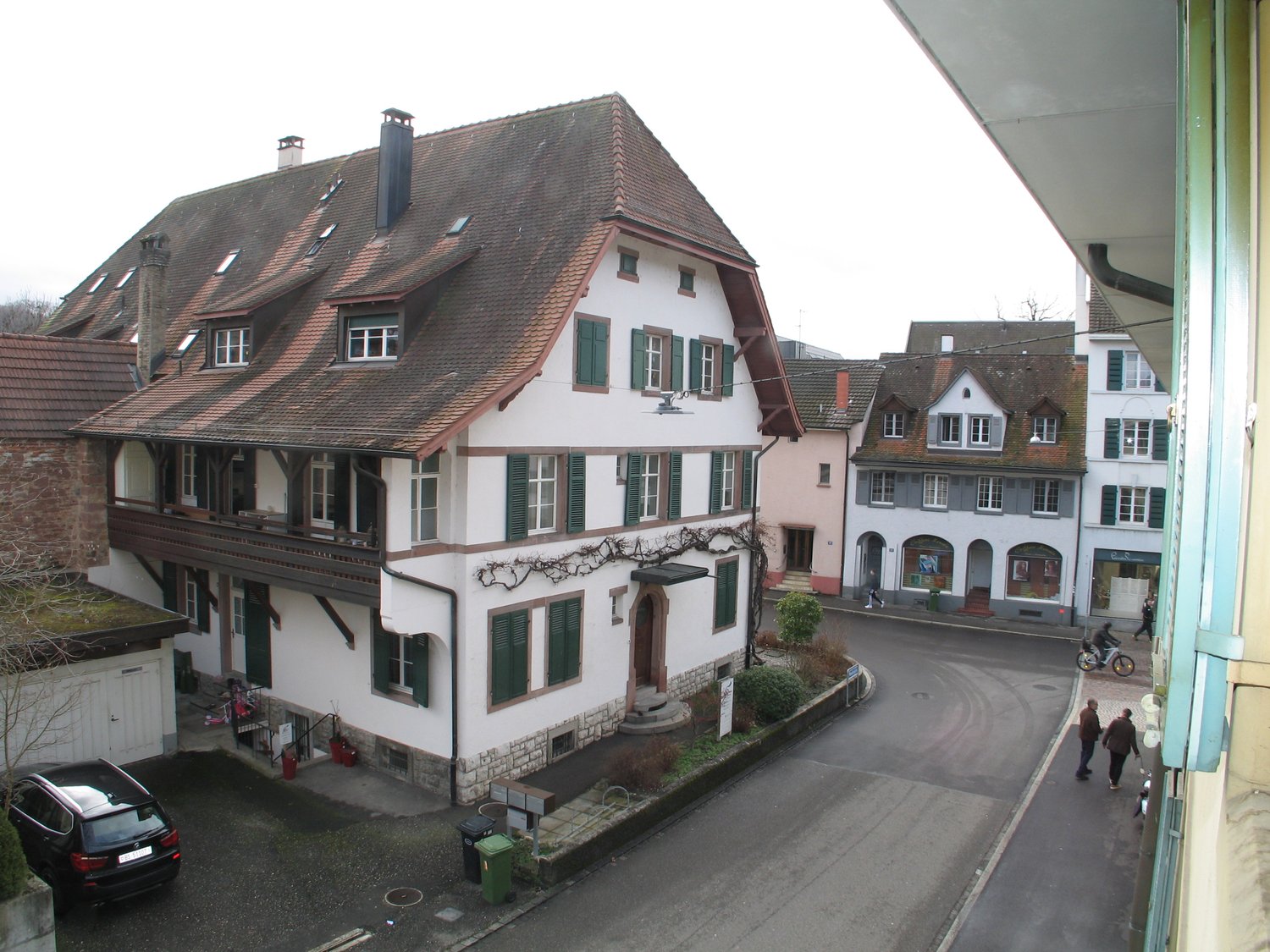 Two story building, brown roof, green shutters, small balcony, parked car
