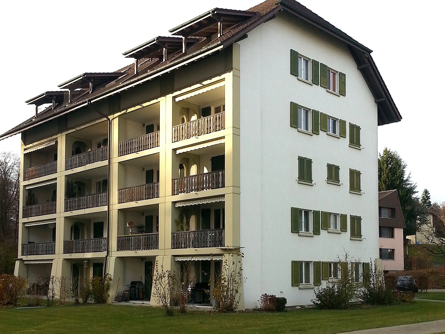Multi-story apartment building, multiple balconies, well-kept garden, windows with green shutters
